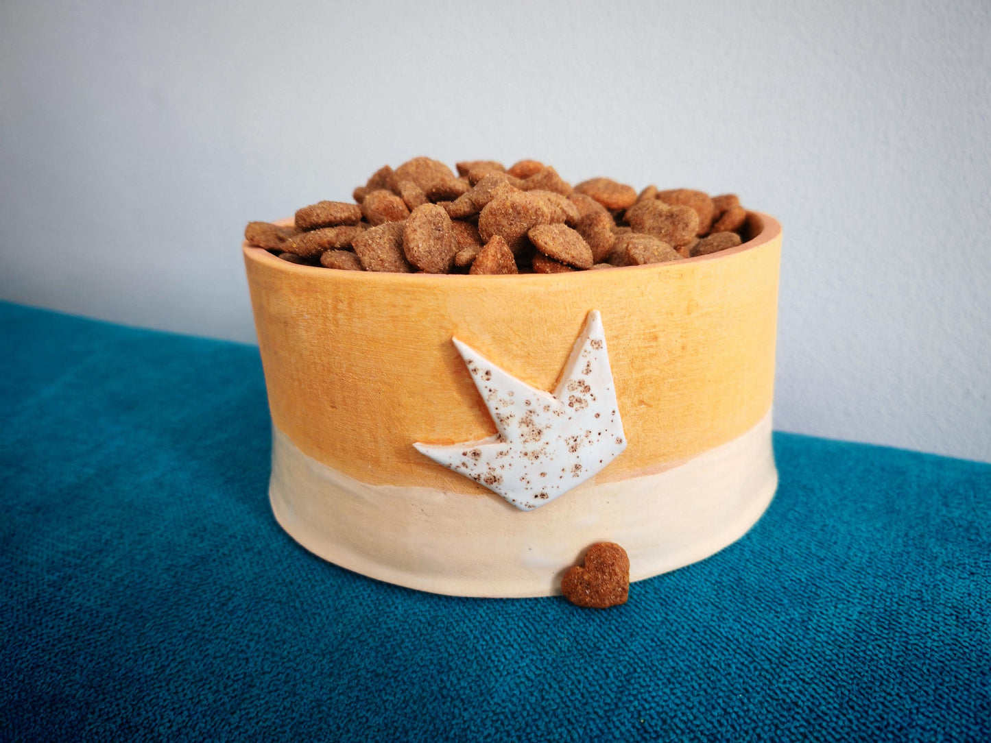 Ceramic orange Dog food bowl with dog food on a blue surface