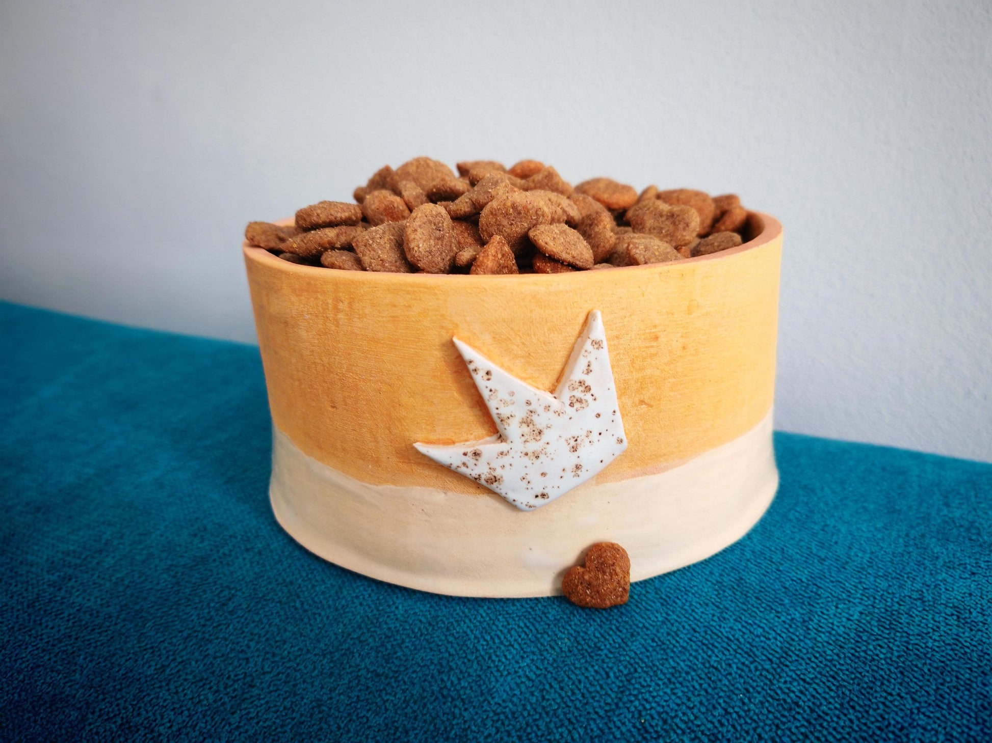 Ceramic orange Dog food bowl with dog food on a blue surface